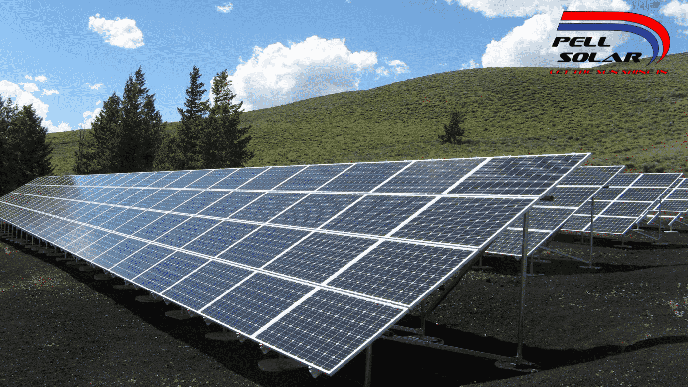 Large solar panels in a grassy field with hills.